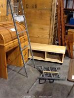 Photo of a gray metal hunting tree stand with an attached ladder and a standing platform. The stand has safety bars and shows signs of surface rust and wear.