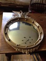 Full view of antique round convex mirror on wooden table showing gold frame with decorative studs.