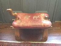 Front view of the camel saddle showing leather seat and decorative wooden legs.