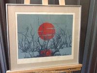 Framed silkscreen artwork showing a red sun and abstract black branches on a blue-grey background.