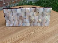 Front view of rectangular handbag made of shiny, square mother-of-pearl shell pieces stitched or linked together forming a glossy mosaic surface.