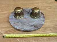 Overall view of the two mounted brass ink wells on oval marble base with measuring tape for scale