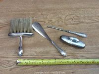 Four antique sterling silver grooming tools laid out with measuring tape showing size reference.