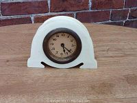Front view of the small French Ivory clock on a wooden surface.
