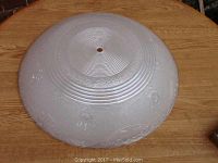 Top-down view of a large circular vintage glass shade cover with concentric rings near the center and textured surface with decorative elements.