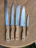 Five St. Jacques knives laid out on wooden surface showing wooden handles and stainless steel blades.