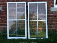 Two white painted wooden storm windows leaning against a brick wall with four glass panes each.