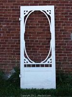 Full view of white wooden screen door with oval cutout and decorative corner accents against brick wall.