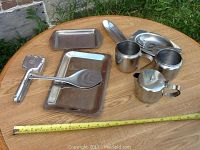 All items displayed on a wooden table outdoors showing overall quantity and scale of the stainless steel serving pieces including trays, cups, ladle, and forks.