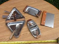 Top view of all serving pieces, showing stainless steel trays with wood accents and accompanying knives and forks placed on wooden surface.