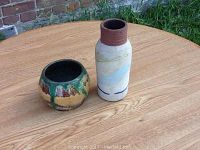 Photo showing two pottery pieces on a wooden table outdoors, small round bowl and tall vase.