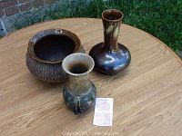 Overview of three pottery pieces: Raku bowl, reddish-brown flared-neck vase, and matte finish vase with twine and beads on table outdoors.