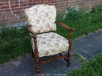 Front view of the wooden armchair showing floral upholstery and carved wooden arms and legs.