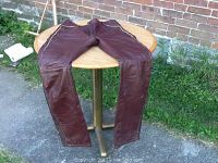 Full length view of the leather motorcycle pants laid flat on a round wooden table outdoors, showing color and general condition.