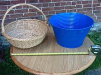 Blue steel tub and wicker basket shown on a round wooden table against a brick wall. Tape measure placed beside items for scale.