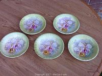 Five small antique plates arranged on a wooden surface, all showing matching floral designs and yellow-green backgrounds.
