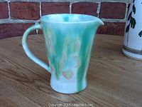 Side view of the mid-century ceramic pouring cup showing green and white glaze, curved spout, and handle.