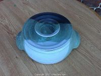 Top view of the covered pottery dish showing its glazed lid with a central knob and two side handles, revealing the color gradient from greenish to dark blue.