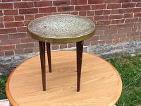 Full view of the small wooden table with brass top, showing the entire table including wooden legs and top.
