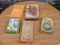 Five boxes of vintage unused greeting cards with floral covers and a 1977 Canadian Old Farmer's Almanac on a wooden table.
