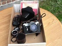 Top view showing the Zenit 35mm camera with strap, an extra Focal lens and leather lens case, and some documents in a box.