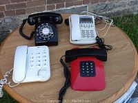 Overview of four telephones on a round wooden surface outdoors showing all four phones in one shot.