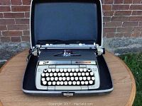 Smith-Corona Classic 12 typewriter fully visible in open carrying case on round table with brick wall background.