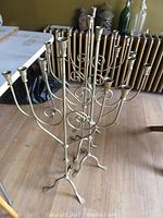Four metal candelabras standing on wood flooring near a radiator, showing overall shape and design with multiple candle arms.