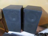 Pair of black rectangular speakers with fabric covers showing wear, standing side by side.