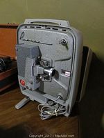 Full view of Revere 8mm movie projector showing front lens, body, power cord, and handle on top.