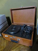 Brown suitcase-style portable record player open and showing turntable and controls.