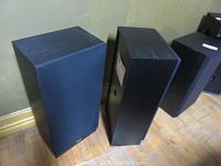 Two black rectangular Accusound speakers with front fabric grilles, standing on a wooden floor showing general wear.