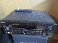 Front view of the black Sony STR-DE985 receiver showing control panel, display, and remote control resting on top.