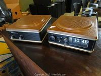 Overall view of Wynford Hall clock radio and stereo adaptor side by side on a wooden surface showing brown textured tops and front controls.