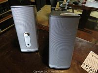 Pair of Bose silver-tone desktop speakers with volume knob visible on right speaker and metal mesh front grille.