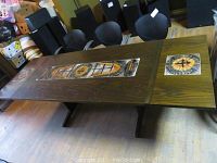 Full view of the rectangular wood dining table with tile inlay centerpiece and one leaf extended on one side, chairs in background.