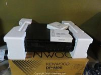 Kenwood DP-M98 multi-CD player unit with original packaging box and manuals on top.