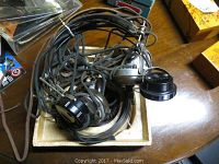 Grouped vintage headphones tangled with cords inside a small tray on a wooden surface.