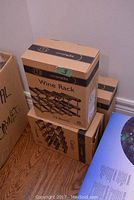 Three cardboard boxes of RTA wine racks stacked, each holding 12 bottles, with visible printed product illustration.