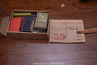 Box with multiple vintage books and folded 1971 Toronto Telegram newspaper with leather belt on floor