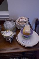 Overview of mixed dishes on wooden table including Nippon cream and sugar set, various plates, candle holders, and napkin holder.
