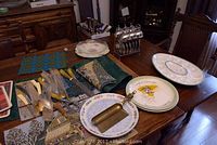 View of assorted kitchen utensils on a wooden table including knives, spoons, parfait spoons, and decorative plates.