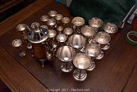 Full view of silver plated teapot with lid, multiple silver plated glasses including aperitif and wine glasses on wooden table