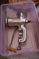 Photo of a Porkert brand metal food grinder with wooden handle, showing the full side view in a plastic bin.