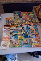 Full view of collection of vintage comic books laid out on table, showing colorful and varied covers of titles including Superman, Batman, Archie, Jughead, Dennis the Menace, Mad in Orbit, Army Laughs, and others.