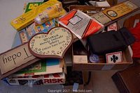 Mixed collection of games, poker chips, cards, Monopoly and Risk board games, signs, and other items spread in boxes on table