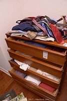 Drawer with assorted clothing including men's shorts, shirts, and ties.