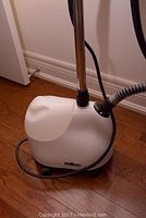 White Salton clothes steamer unit on wood floor showing the main body and cord
