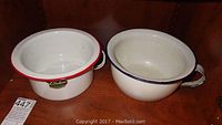 Two vintage enamel bed pans, one with red rim and handle, labeled 'London', the other with blue rim and handle. Both show wear.