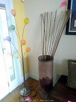 Full view of floor lamp and large decorative vase with bamboo-type decor sticks against wall.